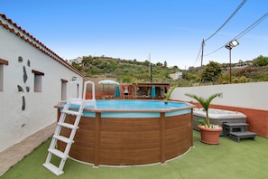 A round swimming pool with a ladder, surrounded by a green artificial turf area.
