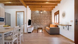 Ein modernes Wohnzimmer mit einer Steinwand, Holzbalkendecke, einem Essbereich mit heller Möbel und einem Fernseher.