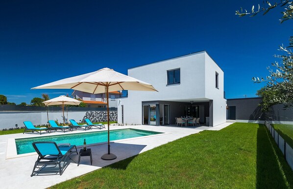 Ein modernes Haus mit Swimmingpool, Sitzgelegenheiten im Freien und einem gepflegten Rasen.