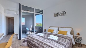 A modern hotel room with a large bed, a balcony with chairs, and a view of the city. - Gorgeous home in Pula (Pula)