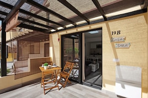 A covered patio with a table and chairs, a sliding glass door leading to a living area, and a wall with a sign indicating room number 19B.