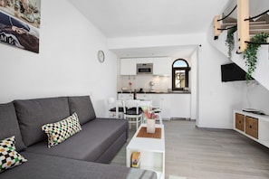 A modern living room with a grey sofa, a coffee table, and a dining area with chairs and a table.