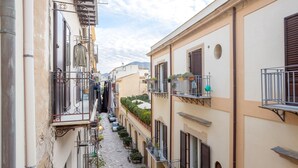 A narrow street with buildings on either side, balconies with railings, and potted plants. - Apartment "La Casa di Faby" with Balcony and Wi-Fi (Palermo)