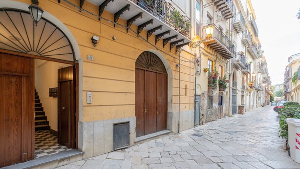 A narrow cobblestone street with historic buildings, wooden doors, and balconies with plants. - Apartment "La Casa di Faby" with Balcony and Wi-Fi (Palermo)