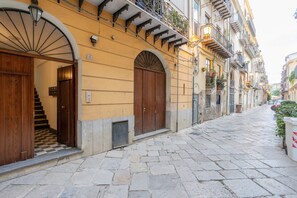 Una estrecha calle adoquinada con edificios históricos, puertas de madera y balcones con plantas.