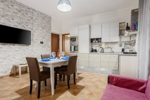 Une cuisine moderne avec des armoires blanches, un four encastré et un téléviseur à écran plat fixé à un mur en briques.