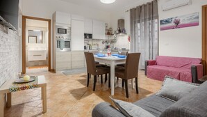 A modern living room with a dining area, a kitchen in the background, and a pink sofa. - Apartment "La Casa di Faby" with Balcony and Wi-Fi (Palermo)