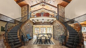 A spacious interior with a central dining area, a stone staircase, and a balcony. - The Meadowbrook, games, BBQ, huge back yard (Big Bear City)
