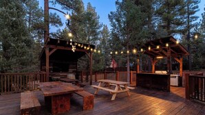 A wooden deck with picnic tables and a covered area, surrounded by trees. - The Meadowbrook, games, BBQ, huge back yard (Big Bear City)