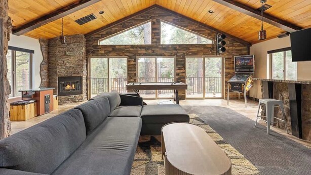A spacious living area with a stone fireplace, a pool table, a large sofa, and a television. - The Meadowbrook, games, BBQ, huge back yard (Big Bear City)