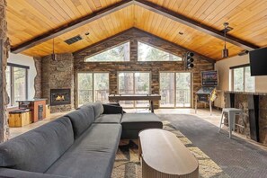 Un amplio salón con chimenea de piedra, mesa de billar, sofá grande y televisor.