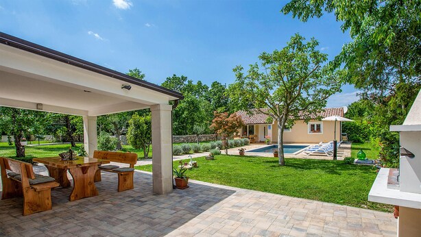 A covered patio with a wooden table and chairs, a swimming pool, and a house in the background. - Nice home in Svetvincenat (Svetvincenat)