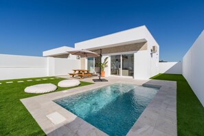 Una casa moderna con piscina, un patio con mesa y sillas, y un césped cuidado.