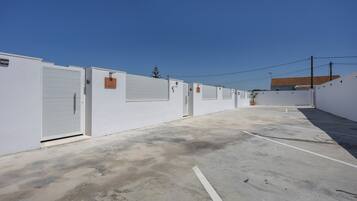 A row of white buildings with closed doors, a clear sky, and a parking area.