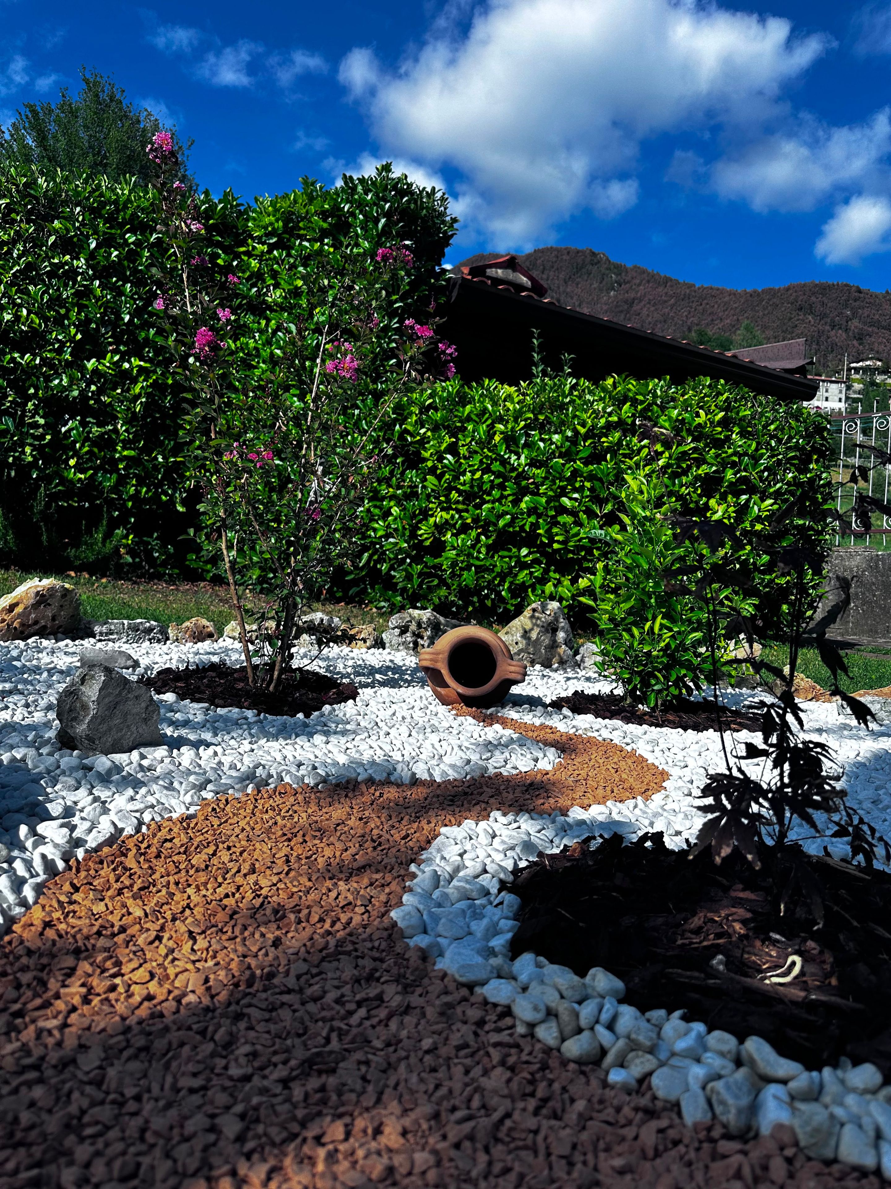 A garden with a variety of plants, a decorative pot, and a patterned ground surface.
