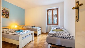 A room with two beds, a window with curtains, a radiator, and a wall-mounted light fixture.