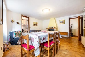 A dining area with a table set for six, surrounded by wooden chairs with pink cushions, a sofa, and a patterned throw.
