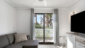 A modern living room with a sofa, a flat-screen TV, and a balcony with a view of palm trees. - Holiday Apartment 'En Playa De Las Americas' with Shared Pool, Private Terrace and Wi-Fi (Playa de Las Americas)
