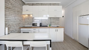 A compact kitchen with white cabinets, a microwave, a sink, and a table with two chairs. - Holiday Apartment 'En Playa De Las Americas' with Shared Pool, Private Terrace and Wi-Fi (Playa de Las Americas)