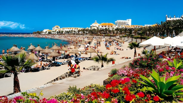 A beach resort with a beachfront, palm trees, and a large building with a yellow roof. - Holiday Apartment 'En Playa De Las Americas' with Shared Pool, Private Terrace and Wi-Fi (Playa de Las Americas)