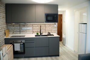 A modern kitchen with grey cabinets, a built-in oven, a microwave, and a refrigerator.