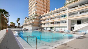 A hotel with a swimming pool, multiple balconies, and a clear sky. - Holiday Apartment 'En Playa De Las Americas' with Shared Pool, Private Terrace and Wi-Fi (Playa de Las Americas)