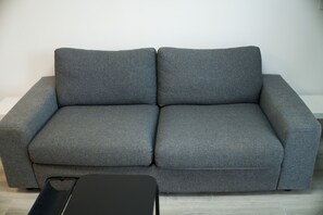A grey sofa with a black side table in a room with light-colored flooring.