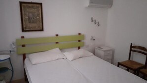 Ein Bett mit grünem Kopfteil, ein Nachttisch, ein Stuhl und eine Wand-Klimaanlage.