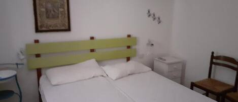 A bed with a green headboard, a bedside table, a chair, and a wall-mounted air conditioner.