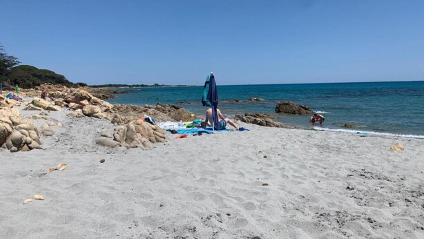 Ein Strand mit Felsen, wolkenlosem Himmel und ruhiger See.