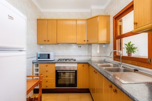 Cocina compacta con armarios de madera, microondas integrado, lavavajillas y pileta de acero inoxidable.