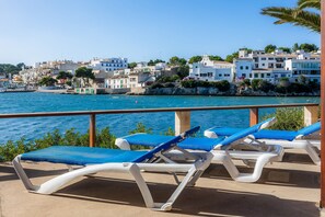 A seaside view with a balcony, blue lounge chairs, and a coastal town in the background. - Holiday Home "Michaela" with Sea View, Private Terrace & Wi-Fi (Santanyi)