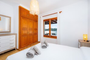 Un dormitorio con un armario de madera grande, una cama con toallas enrolladas, una lámpara de noche y una ventana con vistas.