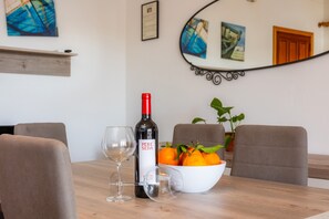 Une table à manger avec une bouteille de vin, des verres et un saladier rempli d’oranges.