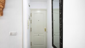 Un pasillo estrecho con una puerta blanca, un teléfono en la pared y un espejo grande.