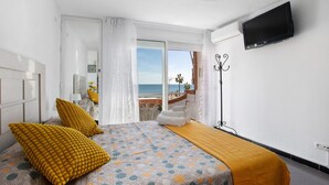 Habitación de hotel con cama, televisión, balcón con vistas al mar y ventana con cortinas.
