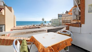 Un balcón con mesa y sillas, con vistas a una playa y edificios.