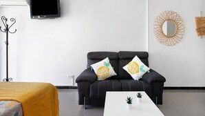Una sala de estar moderna con un sofá, un televisor de pantalla plana, una mesa de centro y un espejo decorativo.