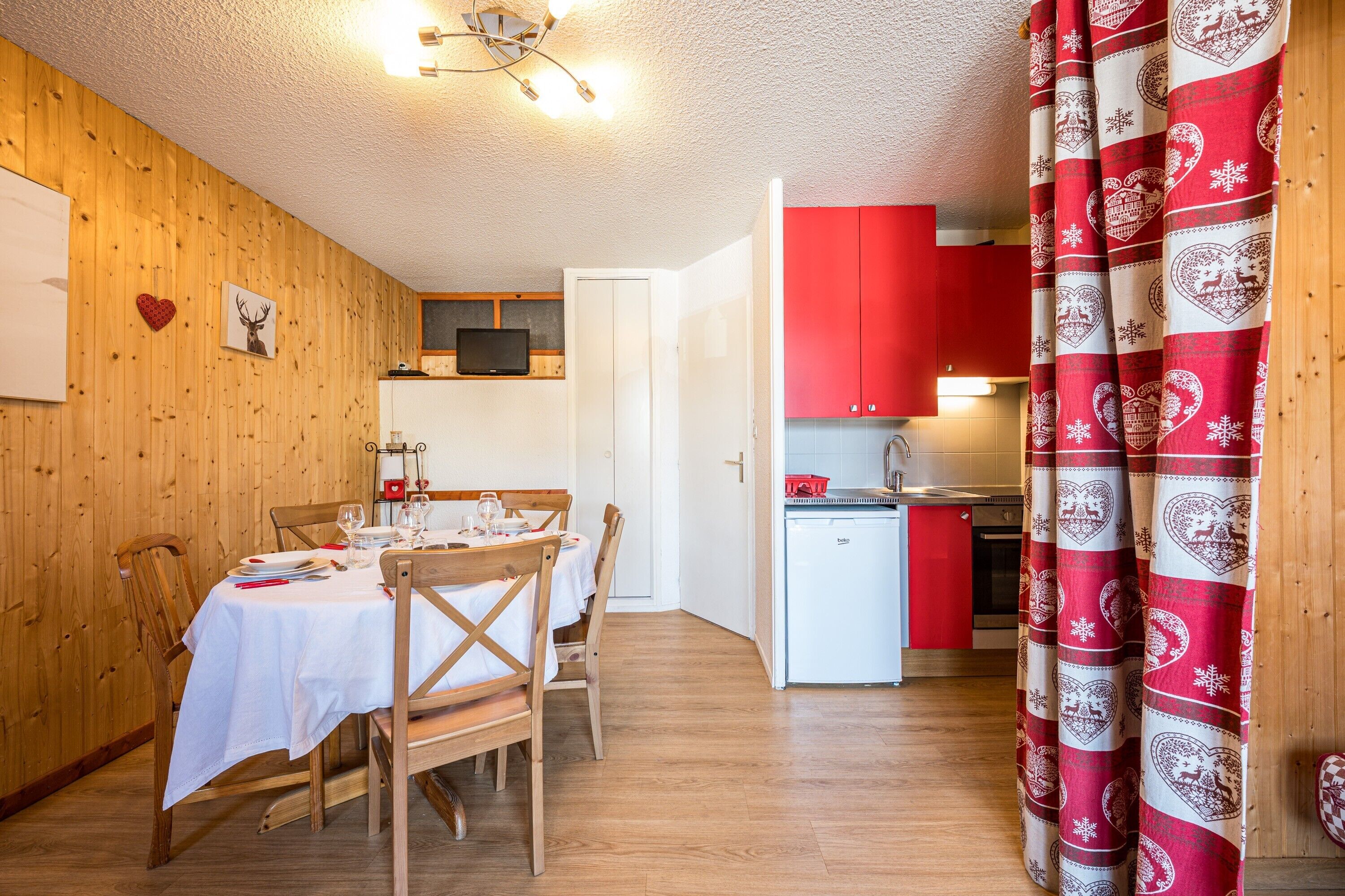 Un comedor con una mesa y sillas de madera, una cocina con armarios rojos y una cortina con estampado rojo y blanco.