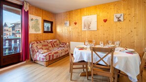 Ein Holzinterieur mit einem für vier Personen gedeckten Esstisch, einer Couch und einem Fenster mit Vorhängen.
