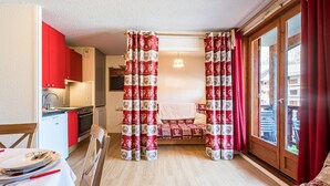 Ein kompakter Raum mit Bett, Essbereich mit Tisch für zwei Personen, Küchenzeile und einer Schiebetür zu einem Außenbereich.