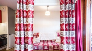 Ein Bett mit gemustertem Überwurf, Vorhänge mit Herz- und Schneeflockenmuster, eine Hängeleuchte und ein Holzboden.