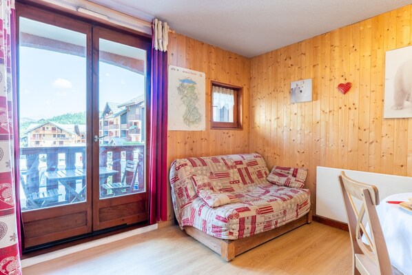 Une pièce en bois avec un canapé, une table, une fenêtre donnant sur des immeubles et une carte accrochée au mur.