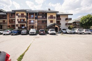 Un hôtel à plusieurs étages, doté de balcons, d’un parking et offrant une vue sur les montagnes.