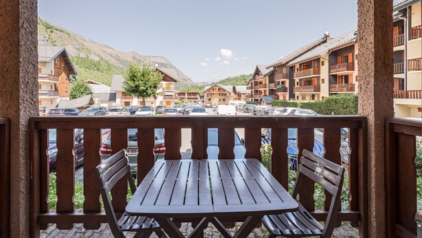 Ein Holzbalkon mit Tisch und Stühlen, der auf einen Parkplatz und Häuser mit Balkonen blickt.