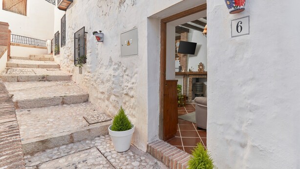 A narrow street with a white building, a staircase, a potted plant, and a door with the number 6.
