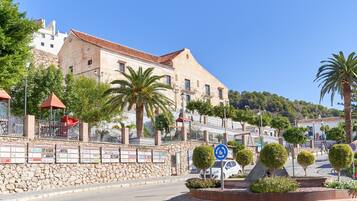 A street with a stone wall, palm trees, and a building with a red roof.