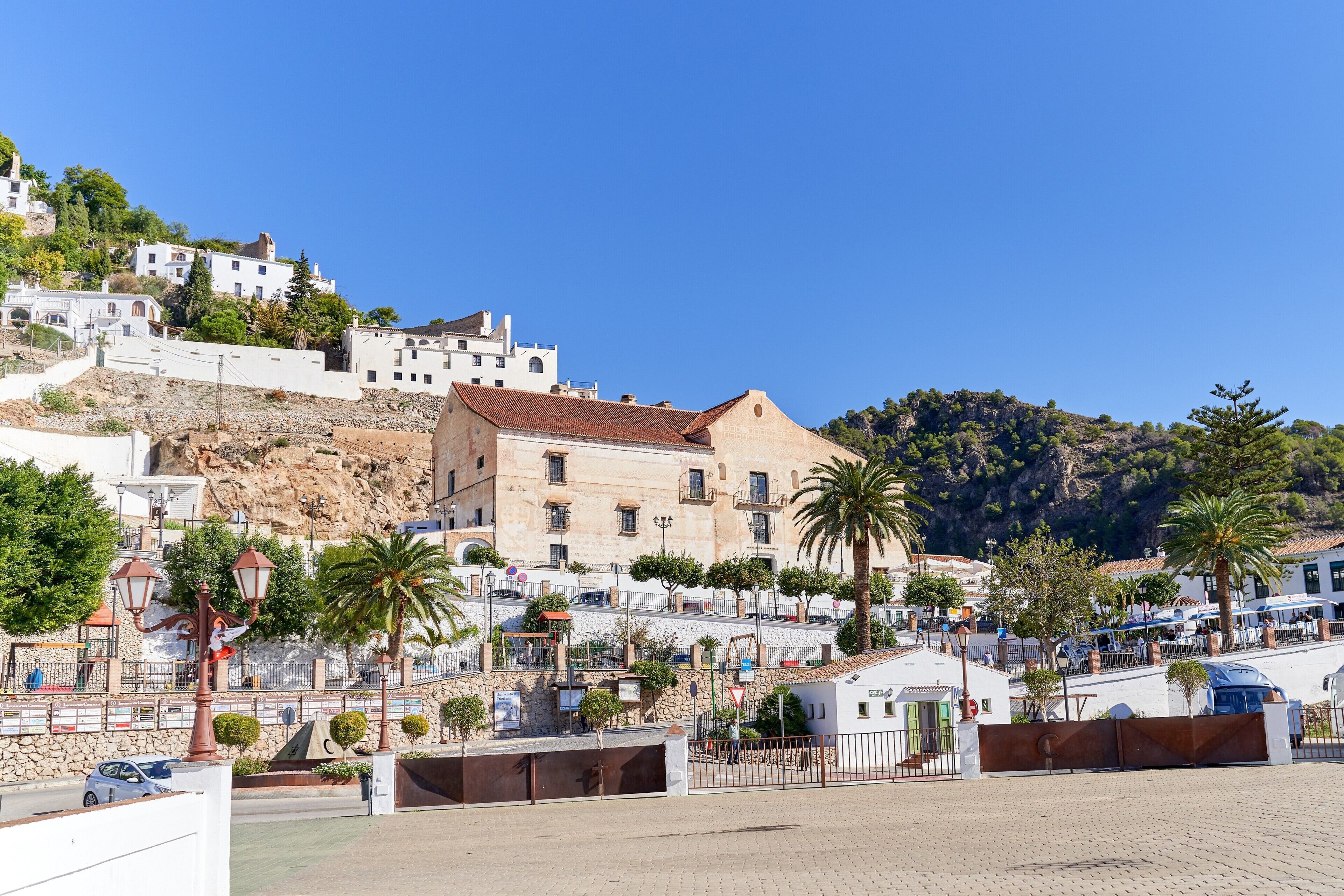 Un pueblo costero con edificios, una plaza empedrada y una colina al fondo.