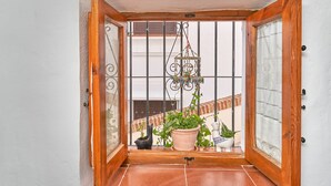 A wooden-framed door with a view of a balcony, a hanging decorative item, and several potted plants.