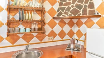 Una cocina con un lavamanos, una cafetera y una alacena con vajilla y tazas.